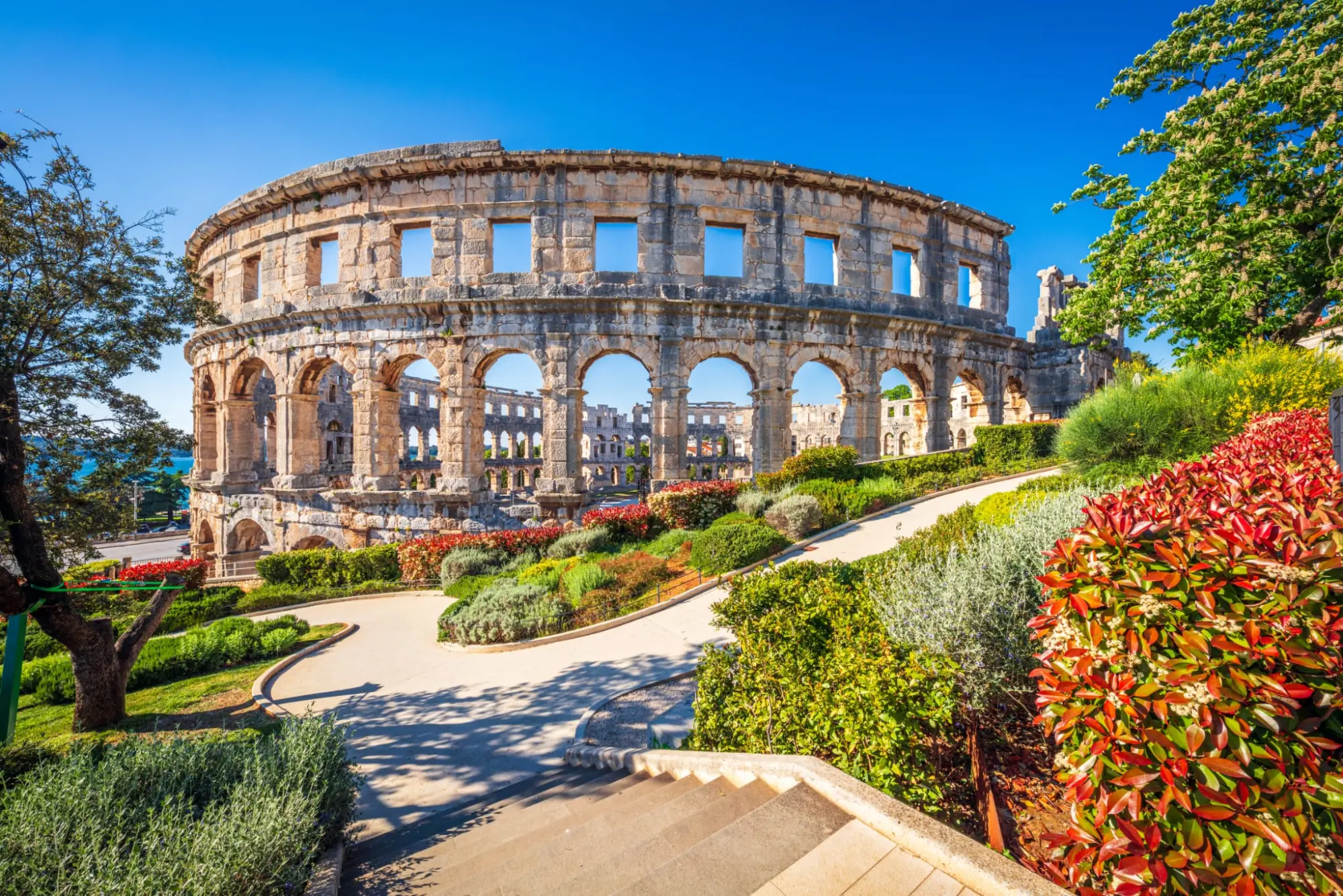 The Pula Arena at golden hour, seen from the garden path